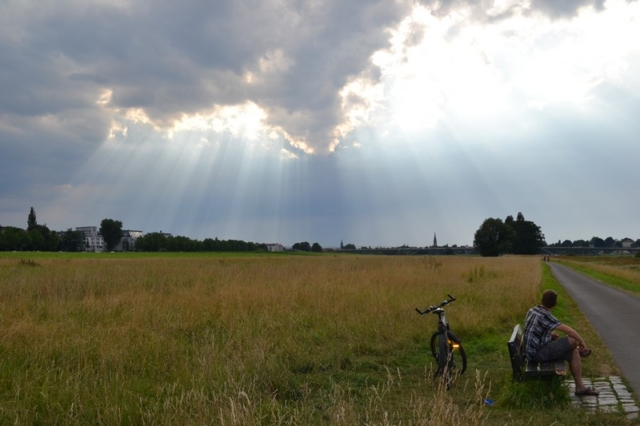 A cyclist rests as sunbeams shine over a Dresden field