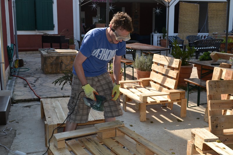 A man building wooden pallet furniture at a hostel